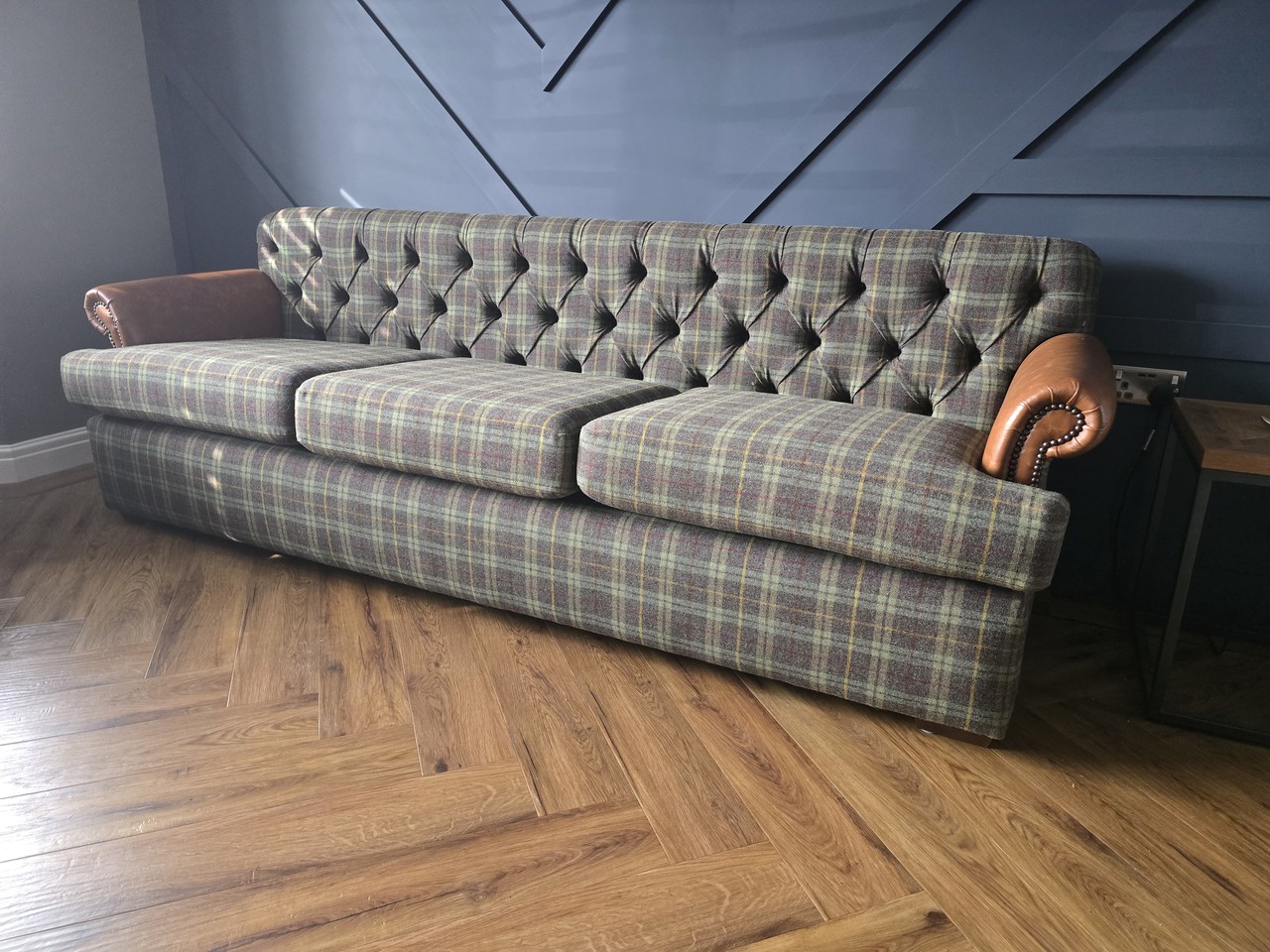 Buttoned tartan sofa with tan arms against a blue wall
