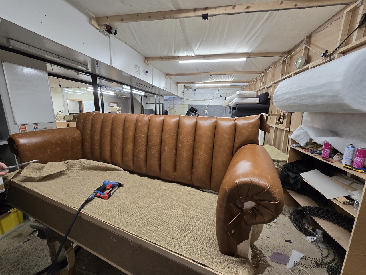 Partly upholstered tan sofa on a workbench with an upholstery tool